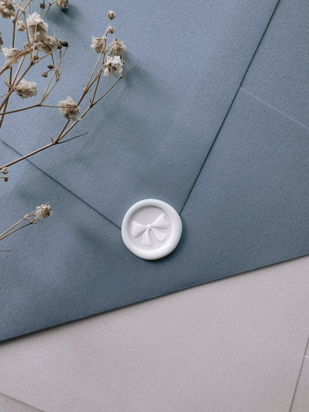 white mini ribbon bow wax seal on a dusty blue envelope