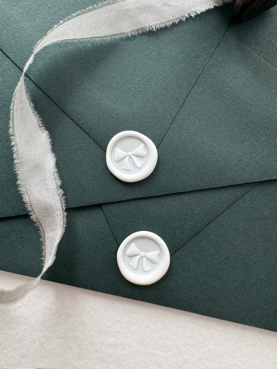 two white 3D ribbon bow mini wax seals on two dark green envelopes 