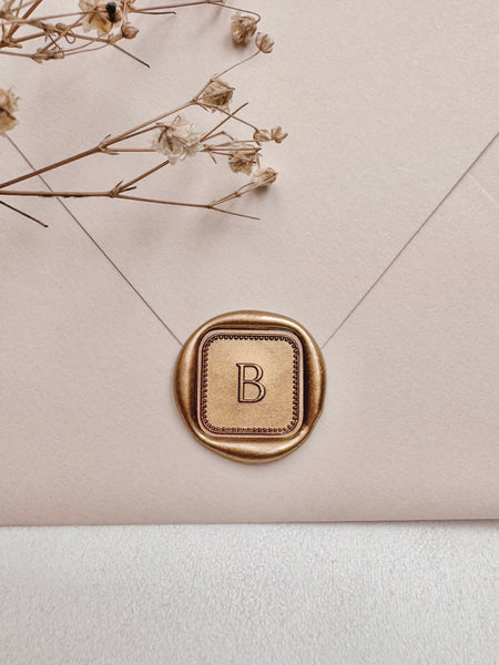 Single initial with border design mini square gold wax seal on a beige envelope