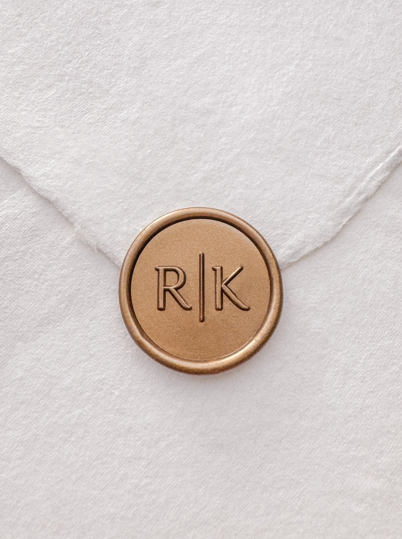 Typeface monogram gold wax seal on a white handmade paper envelope