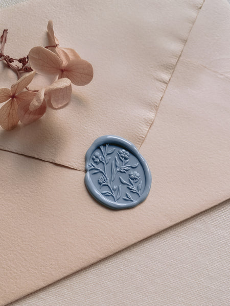 Oval floral wax seal with 3D engraving in dusty blue on light orange handmade paper envelope styped with dried hydrangea petals