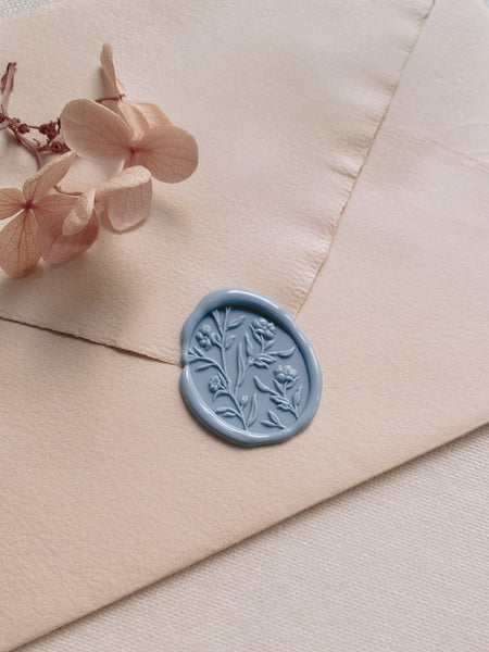 Floral pattern oval dusty blue wax seal on a pale salmon colored envelope