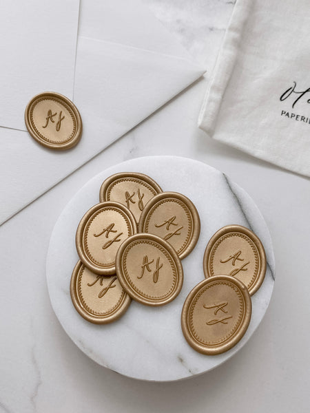 Border monogram oval gold custom wax seals in gold on small gray stone dish