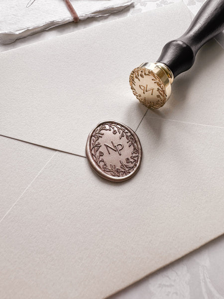 Floral wreath design monogram oval wax seal in a light bronze color on a beige envelope