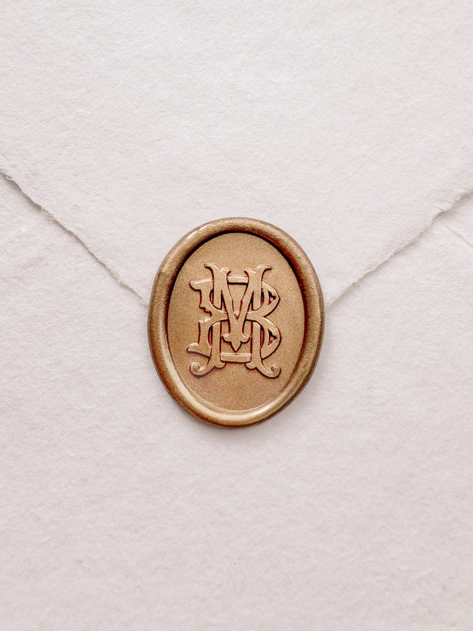 Oval vintage monogram gold wax seal on a white handmade paper envelope