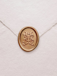 Oval vintage monogram gold wax seal on a white handmade paper envelope