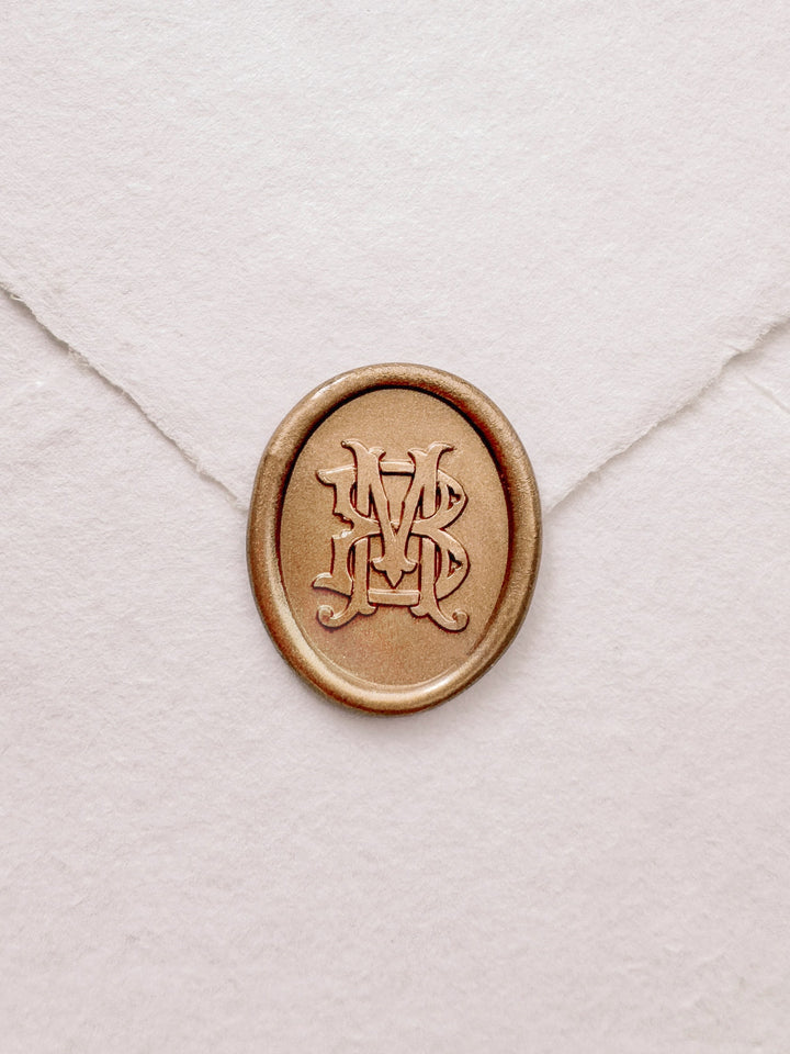 Oval vintage monogram gold wax seal on a white handmade paper envelope
