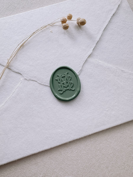 Green oval vintage monogram wax seal on a white handmade paper envelope