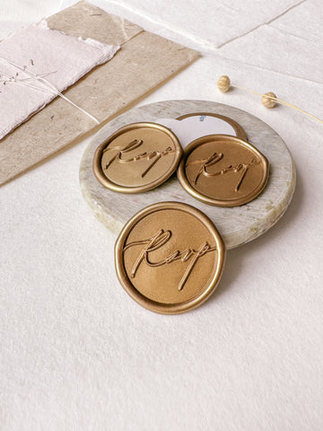 Calligraphy script "RSVP" gold wax seals styled with a small gray stone dish, handmade paper and a dried floral branch