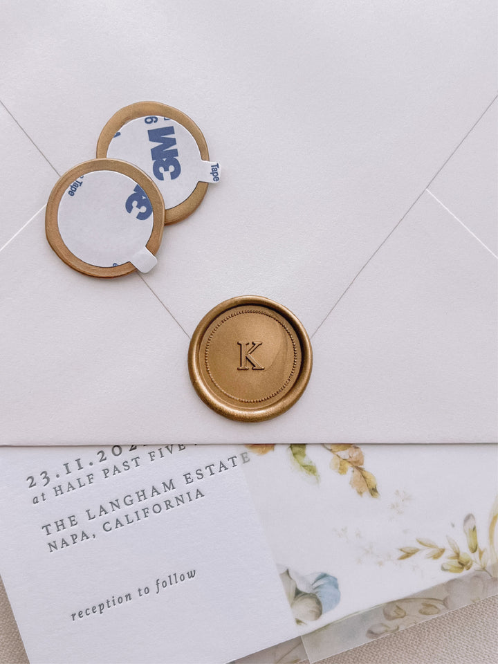 Gold custom monogram with dot border wax seal stickers with self-adhesive backings on a wedding invitation card, beige envelope, and vellum jacket