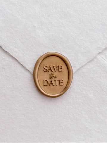 Gold Save The Date oval wax seal on a white envelope