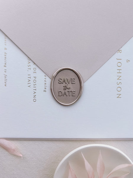 Light bronze save the date oval wax seal on a white wedding invitation card with a pale pink envelope
