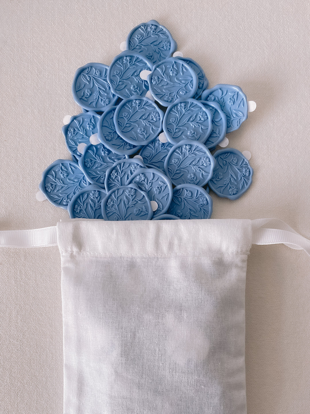 Dusty blue floral wax seals with 3D engraving attached with 3M adhesive backings placed in white linen pouch