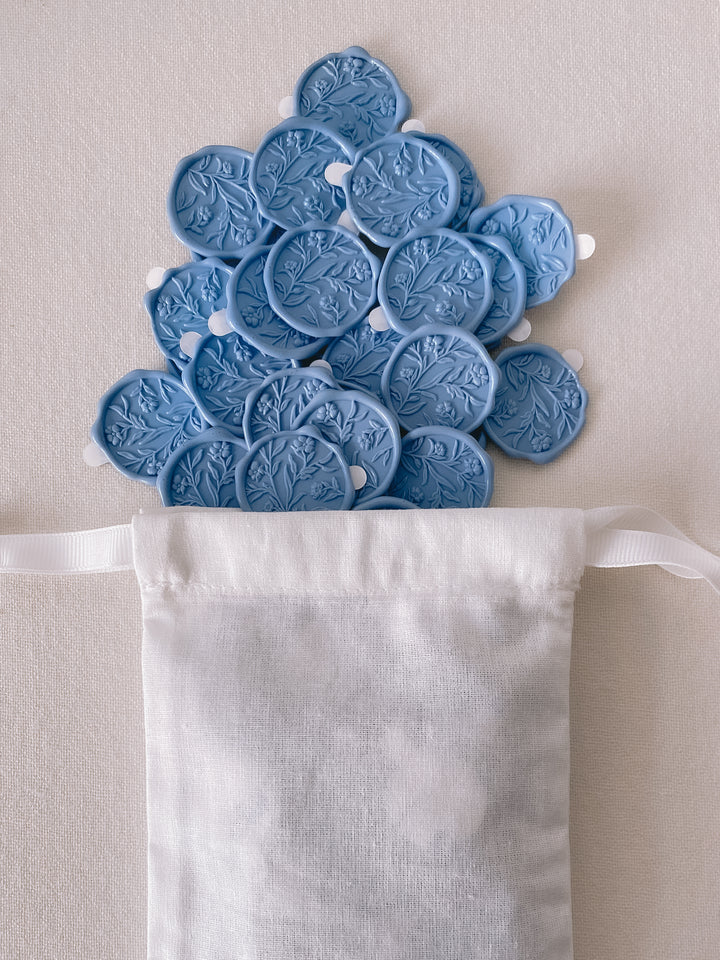 Dusty blue floral wax seals with 3D engraving attached with 3M adhesive backings placed in white linen pouch