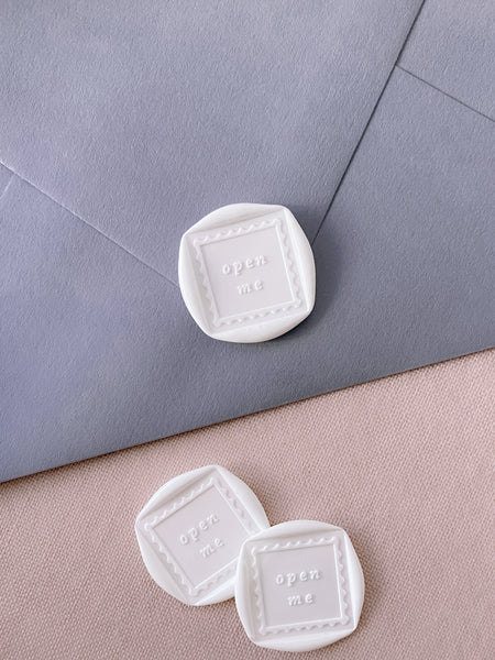 white square shaped wax seals featuring the phrase "open me"