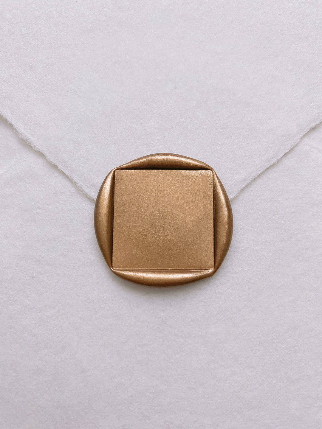 Square blank gold wax seal on white handmade paper envelope