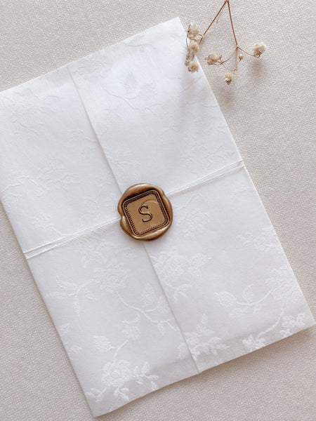 Single initial with border design mini square gold custom wax seal on white floral vellum wedding invitation wrap with twine