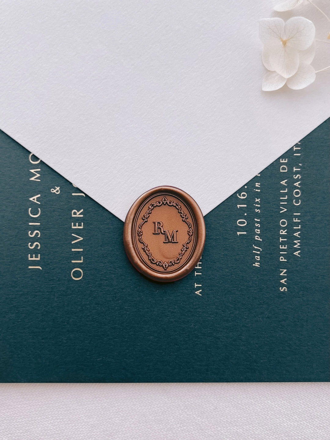 Bronze vintage ornate frame personalized initials wax seal on a beige envelope over a dark green wedding invitation card