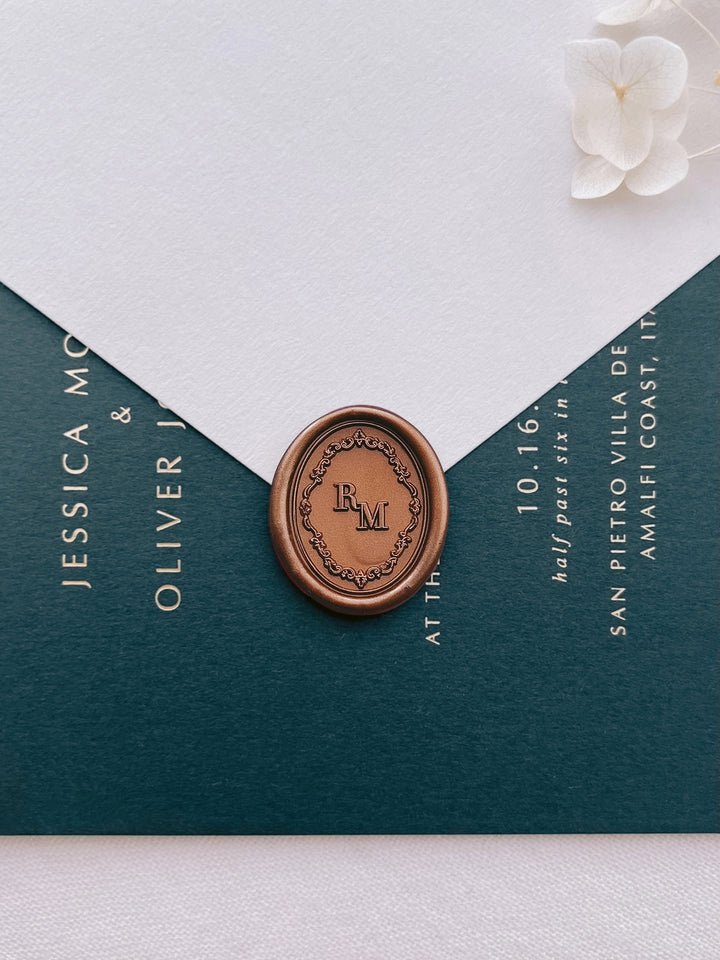 Bronze Baroque vintage crest custom monogram oval wax seal on a beige envelope over a dark green wedding invitation card