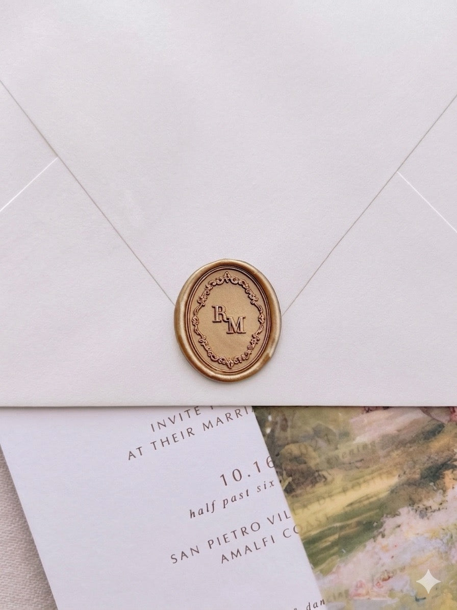 Personalized initials vintage monogram wax seal featuring a Baroque crest border on a beige envelope over a wedding invitation card and vellum jacket