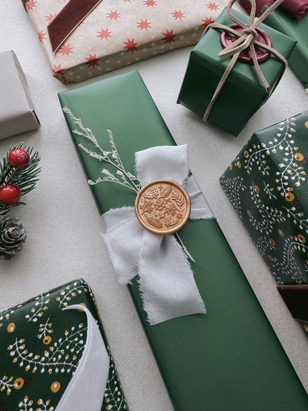 Peachy gold festive winter botanical wax seal on a gift wrapped in green festive wrapping paper and tied in a white silk ribbon