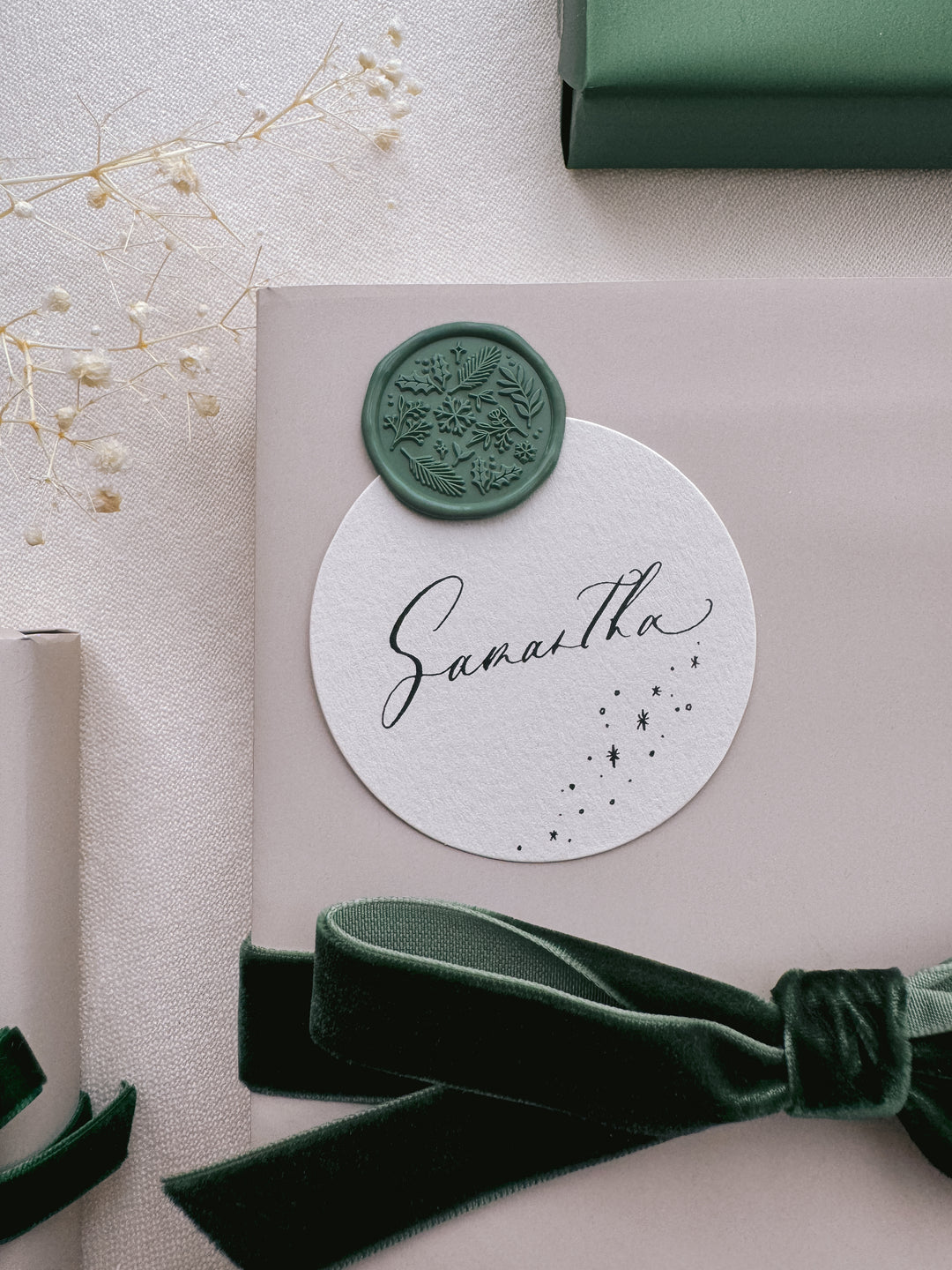 Green winter garden botanicals wax seal on a personalized name tag on a gift wrapped in beige wrapping paper and tied in a dark green velvet ribbon