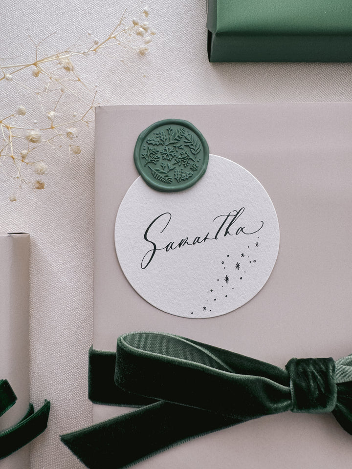 Green winter garden botanicals wax seal on a personalized name tag on a gift wrapped in beige wrapping paper and tied in a dark green velvet ribbon