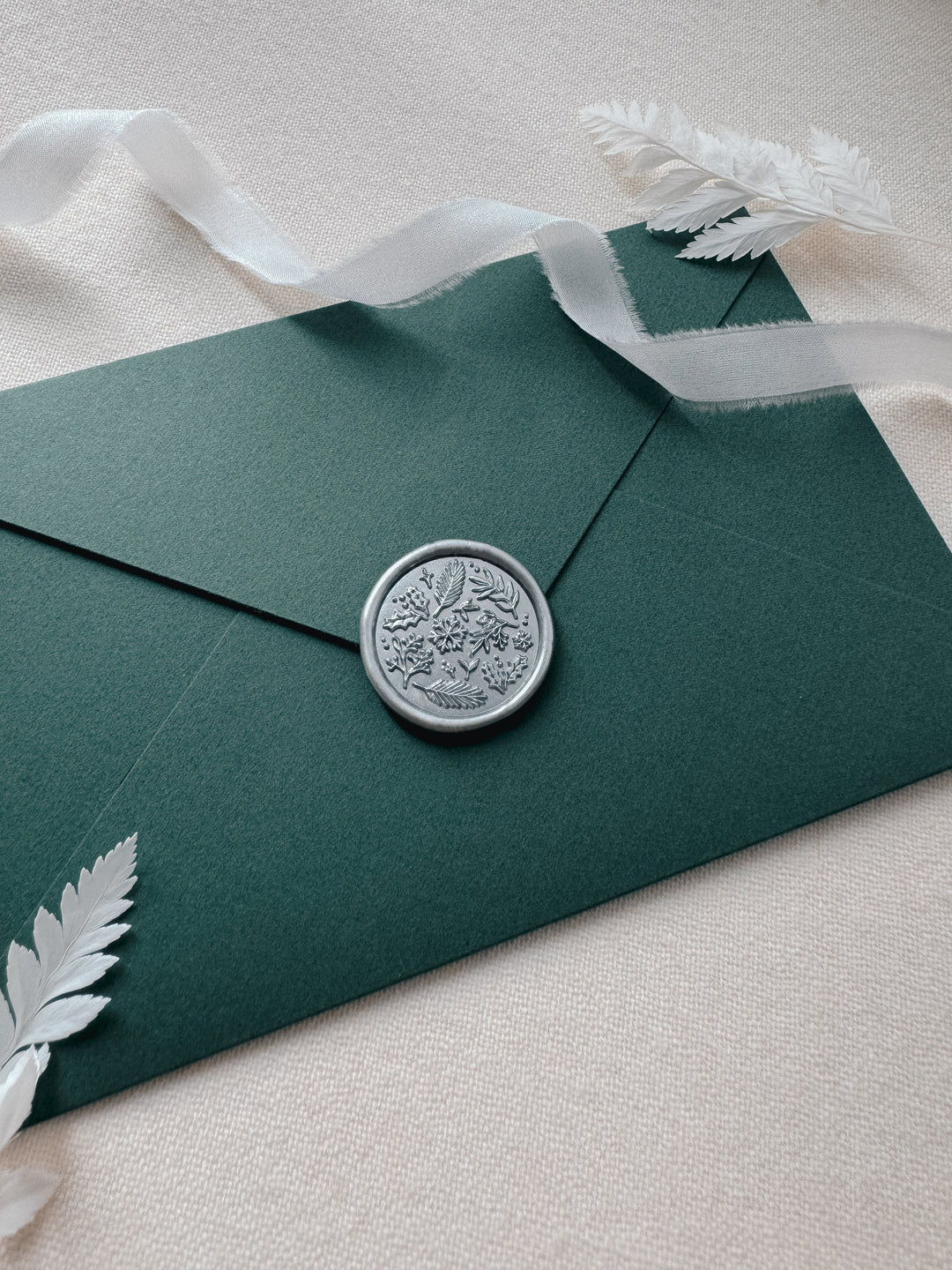 Silver wax seal featuring winter leaves and snowflake, on a dark green envelope