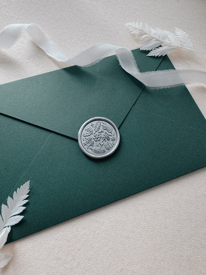 Silver wax seal featuring winter leaves and snowflake, on a dark green envelope