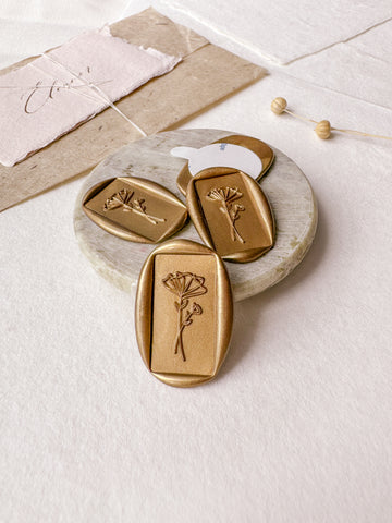 Floral rectangular gold wax seals styled with a small gray stone dish, handmade paper and a dried floral branch