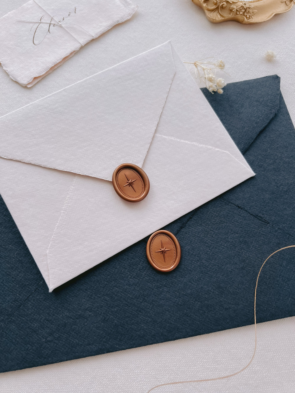 Dark metallic bronze 3D north star mini oval wax seals on a white and black textured envelopes