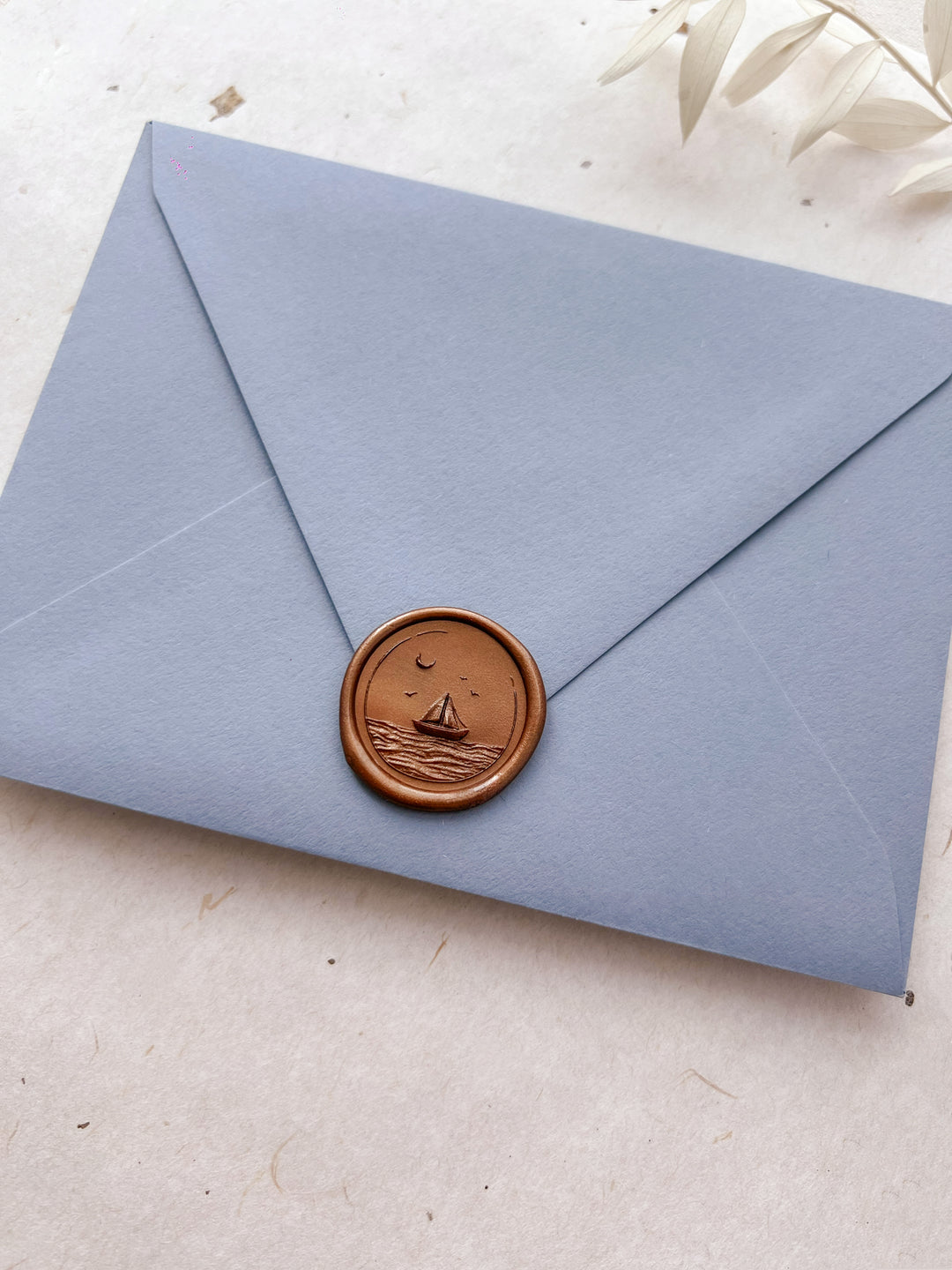 antique gold colored coastal wax seal featuring a sailboat and ocean waves 3D design on a dusty blue envelope