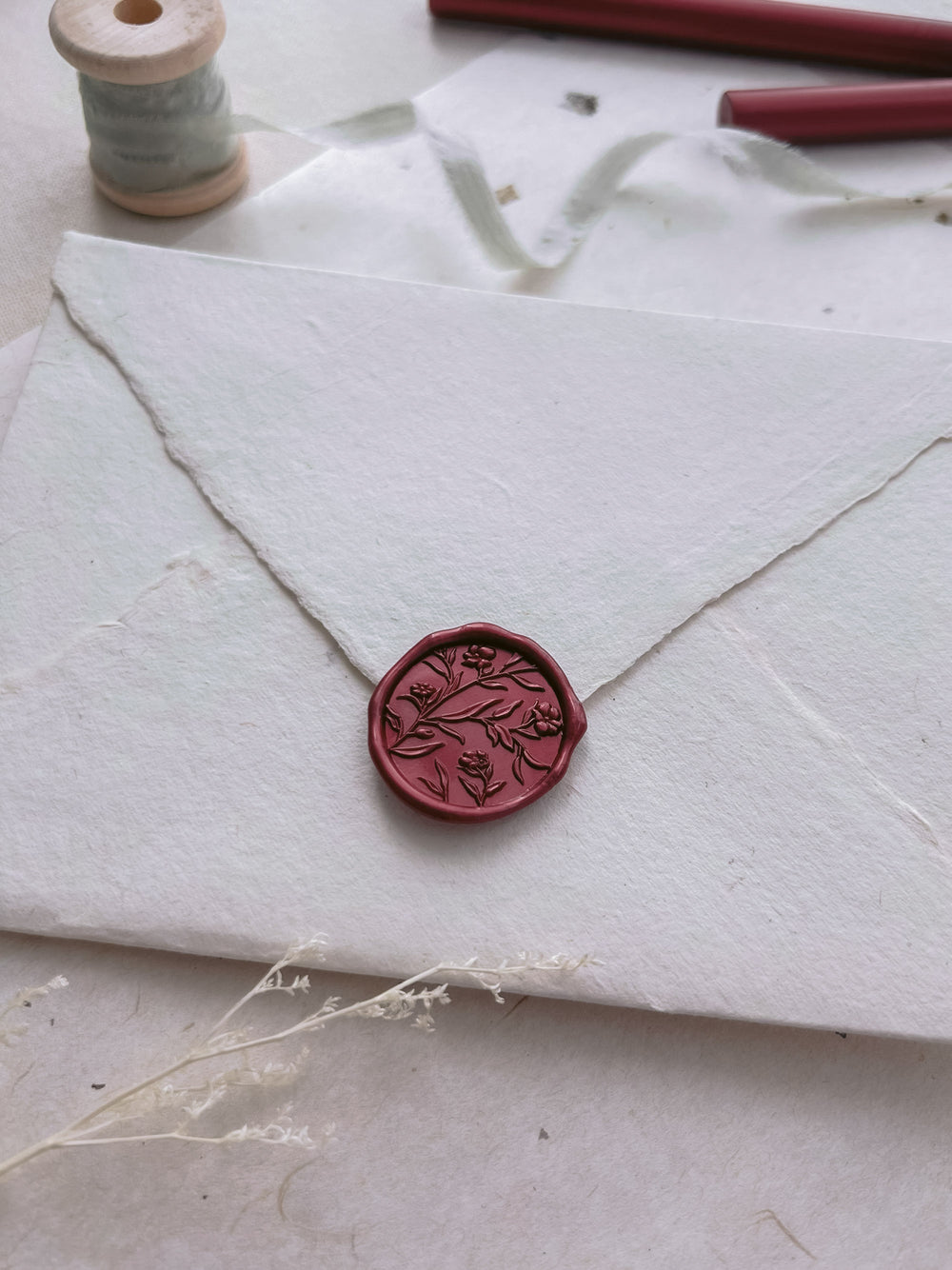 Dark metallic red floral design wax seal on a white envelope