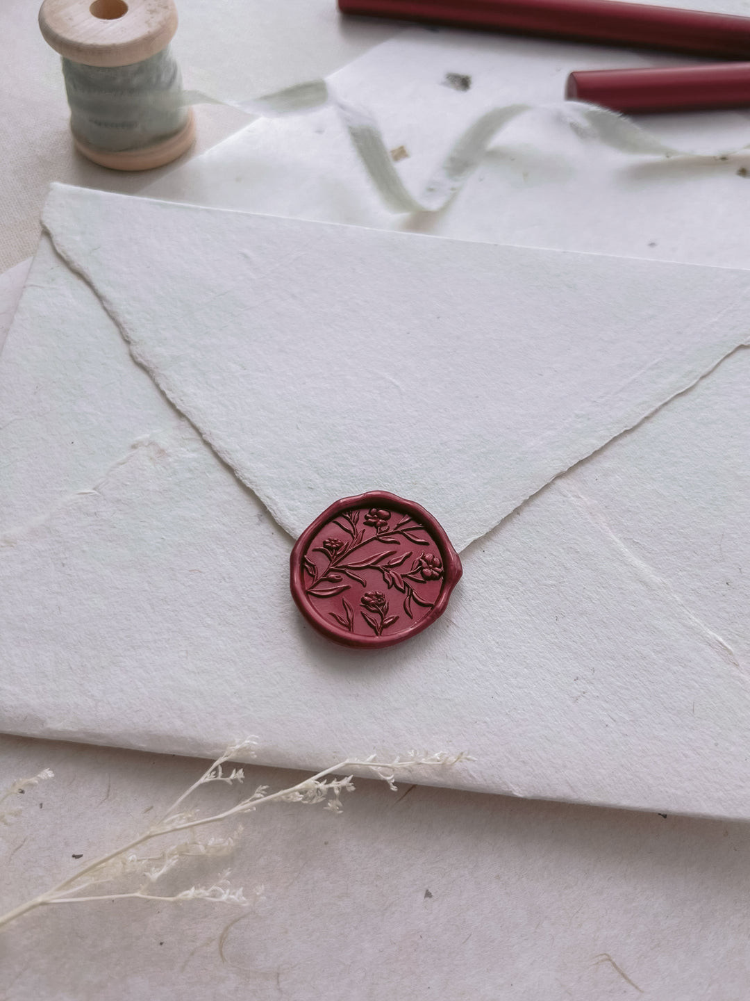 Dark metallic red floral design wax seal on a white envelope