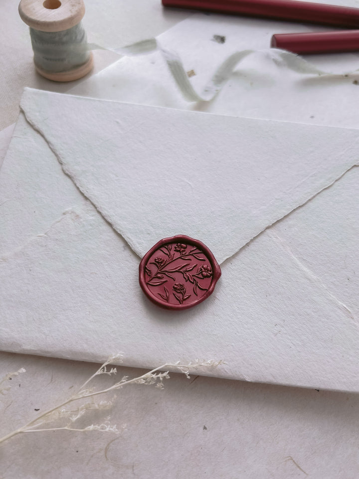 Dark metallic red floral design wax seal on a white envelope