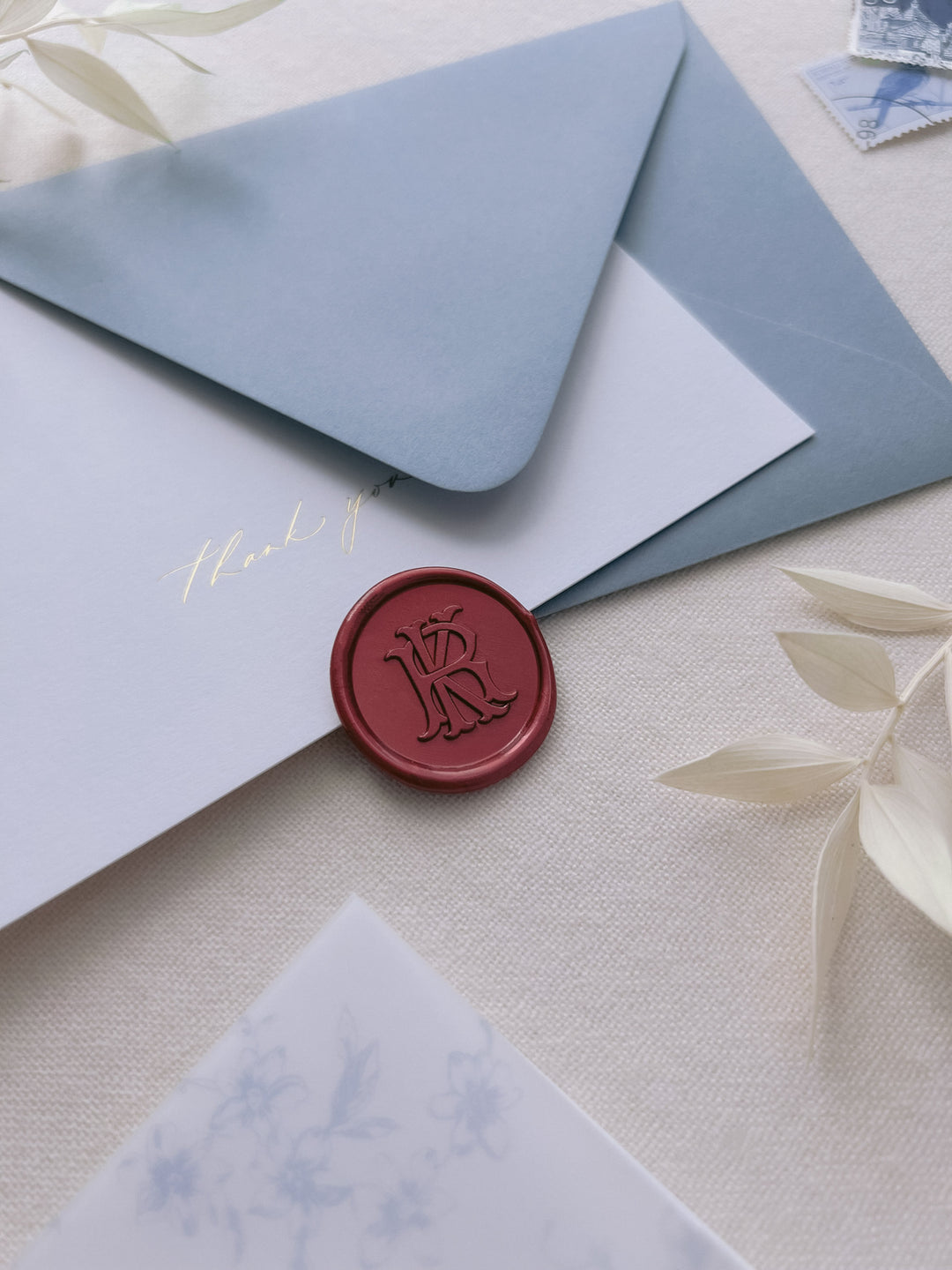 Dark metallic red vintage interlocked monogram wax seal on a dusty blue envelope