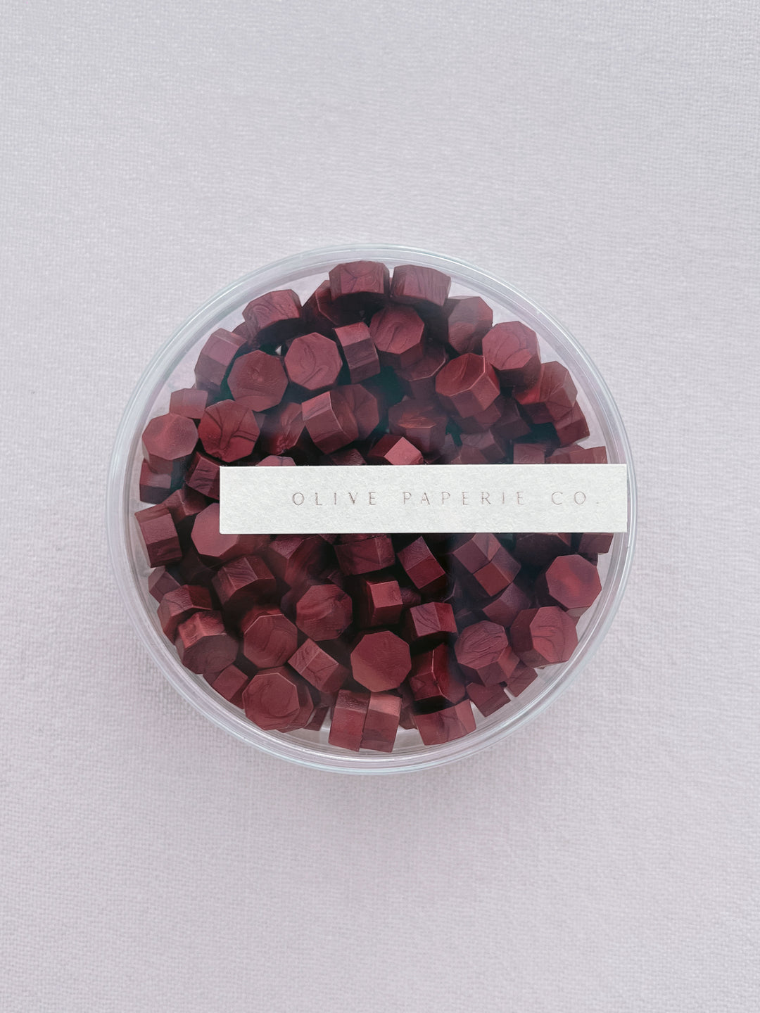 Deep metallic red sealing wax beads in a clear round container