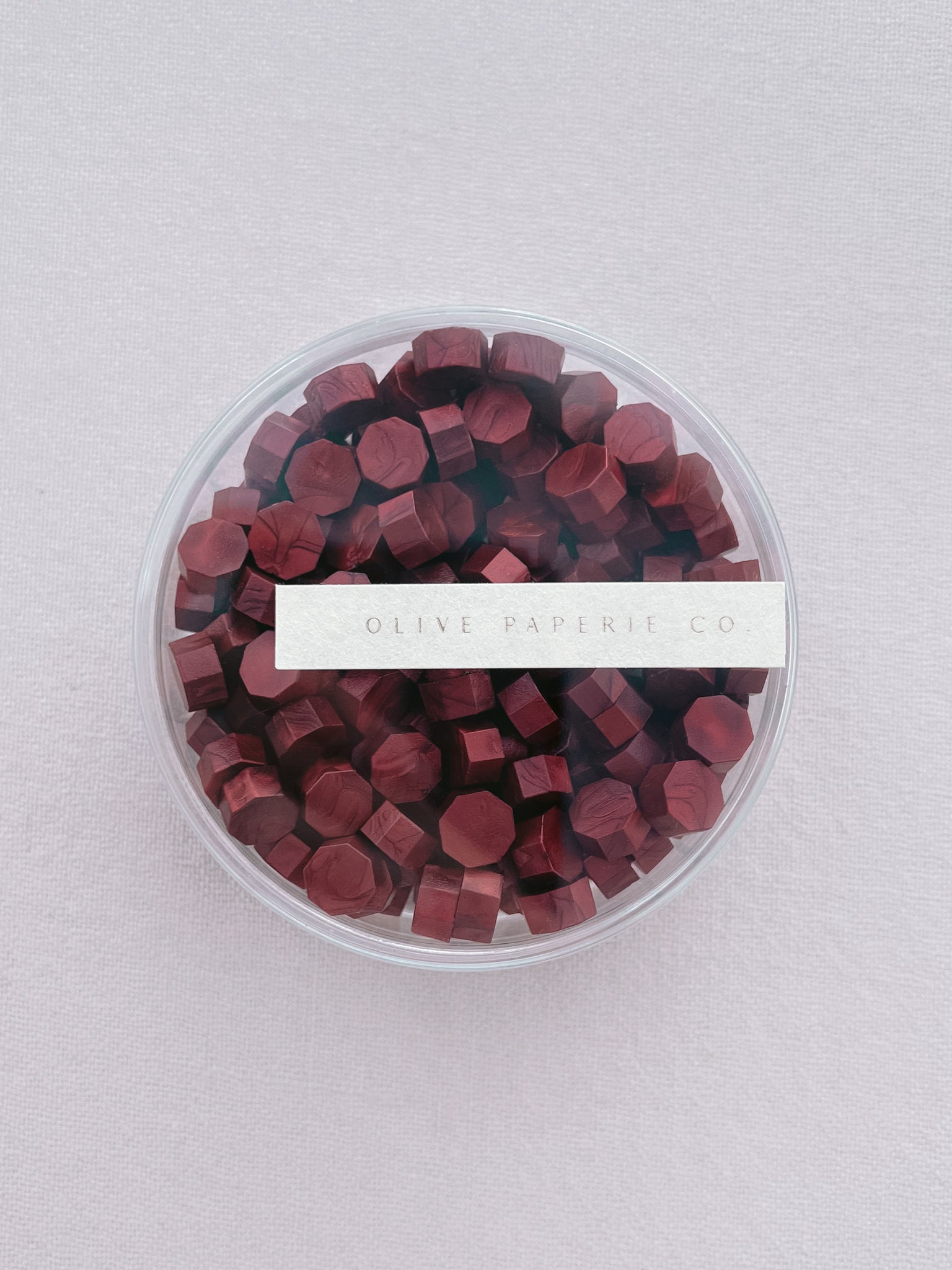 Deep metallic red sealing wax beads in a clear round container
