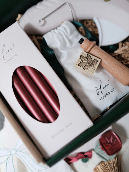 Pack of 5 dark metallic red sealing wax sticks placed next to a festive holly leaf wax stamp and glue gun