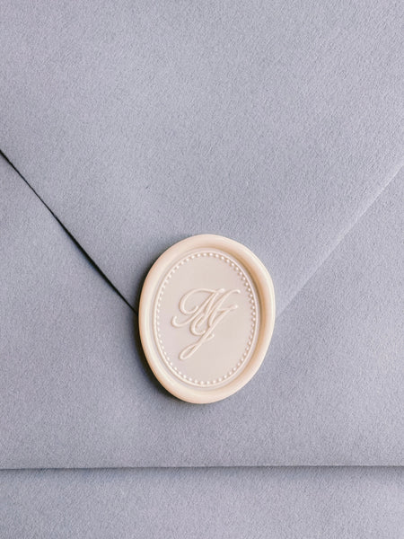 Off-white oval custom monogram wax seal with border design on a light grey envelope
