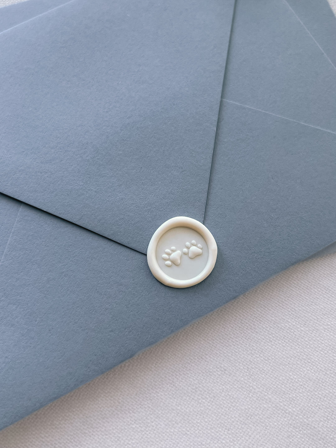 An off-white 3D paw prints mini wax seal on a dusty blue envelope
