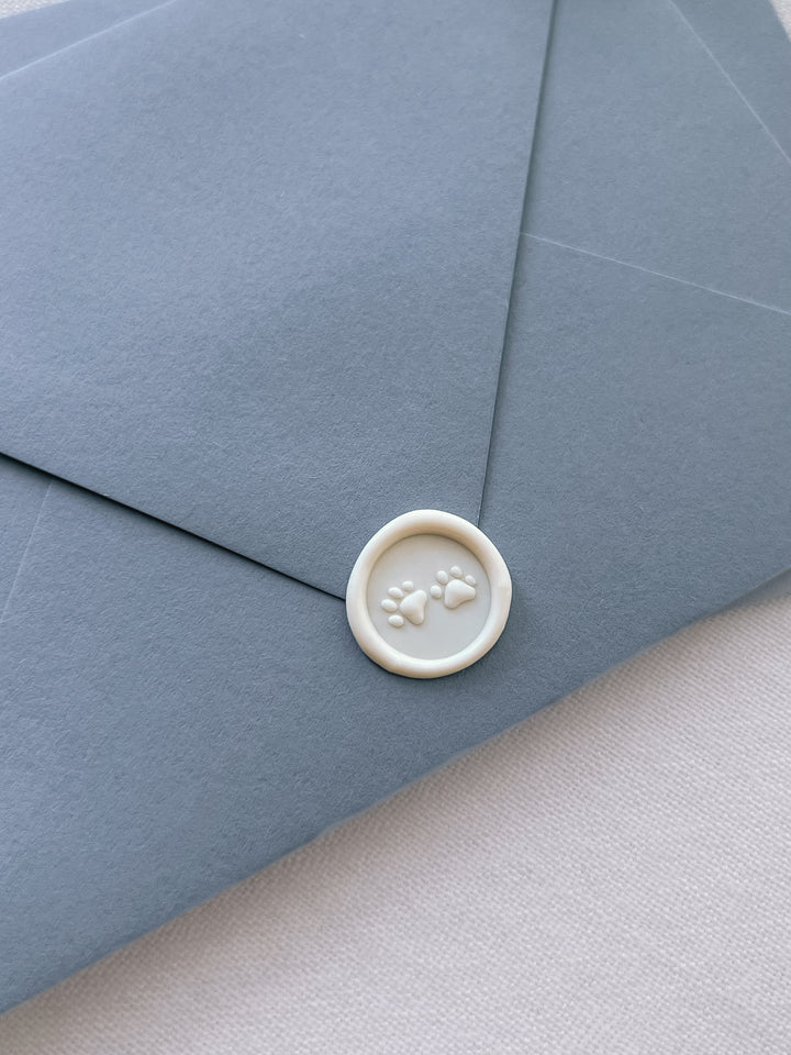 An off-white 3D paw prints mini wax seal on a dusty blue envelope