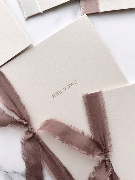 Her Vows beige card stock vow books in typeface font printed in gold foil tied in brown colored silk ribbon