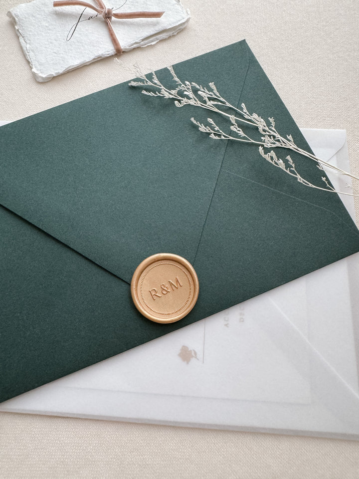 Light gold personalized monogram border wax seal featuring custom initials on a dark green envelope and wedding invitation vellum envelope 