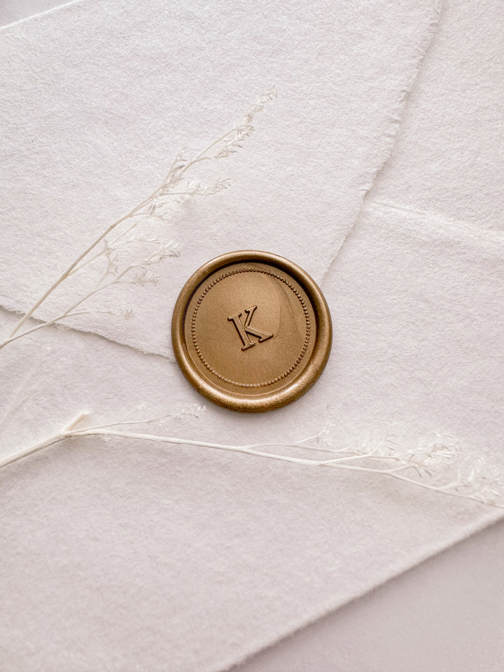 Gold personalized initial border design wax seal featuring a custom monogram on a white deckled edge handmade paper envelope