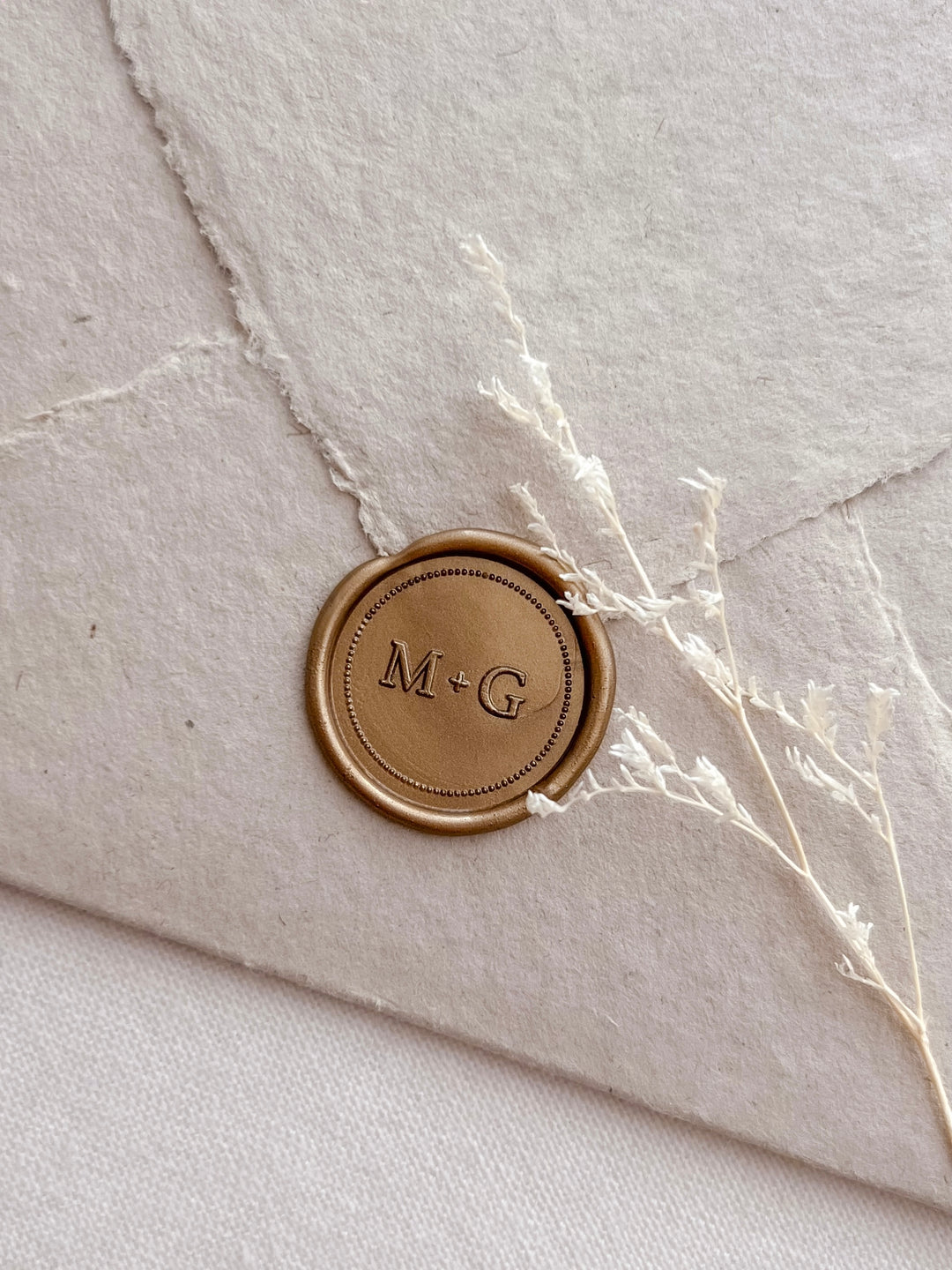 Personalized initials and border design gold wax seal featuring a custom monogram on a light beige textured envelope