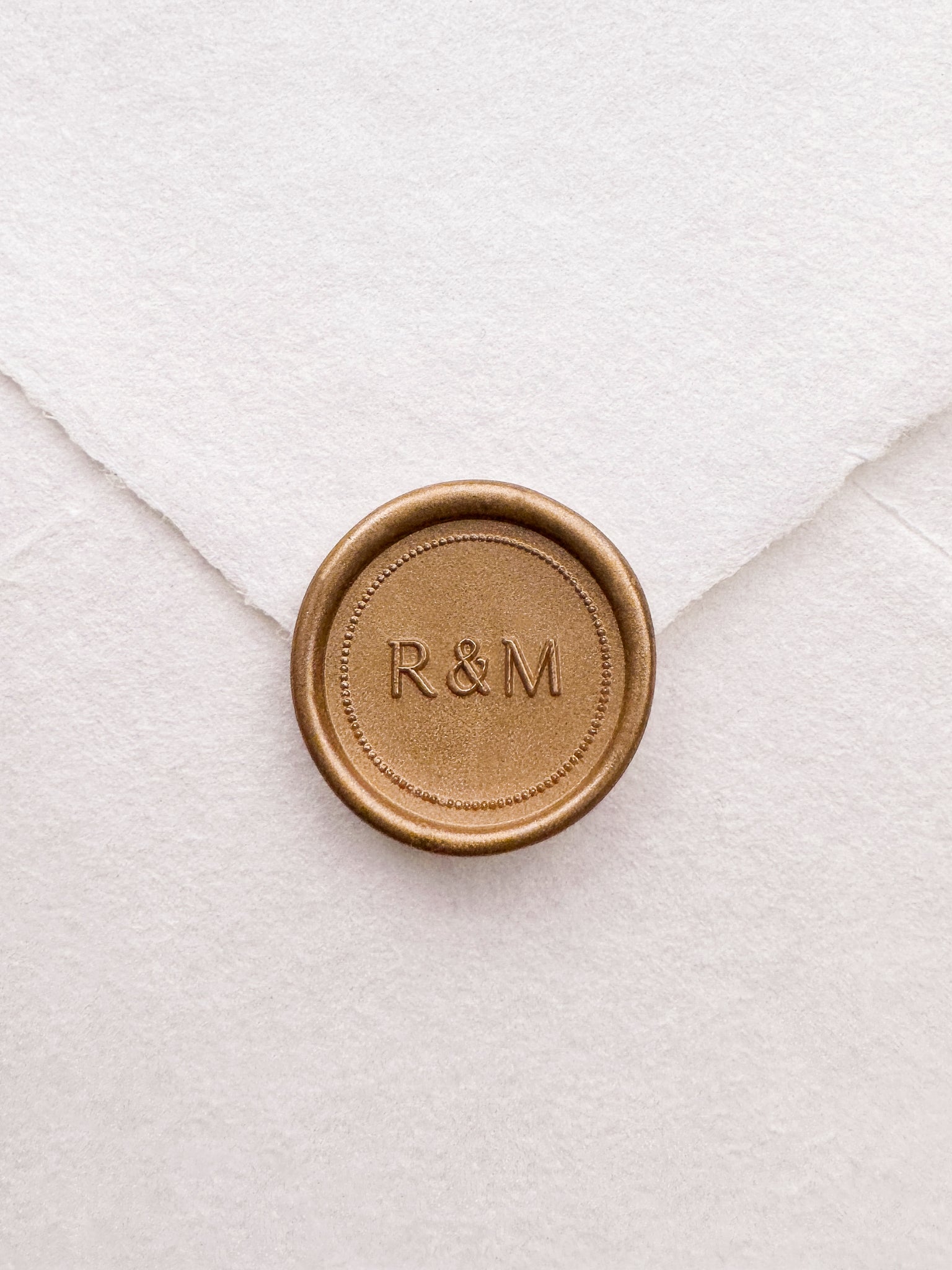 Gold monogram wax seal with a dotted border design