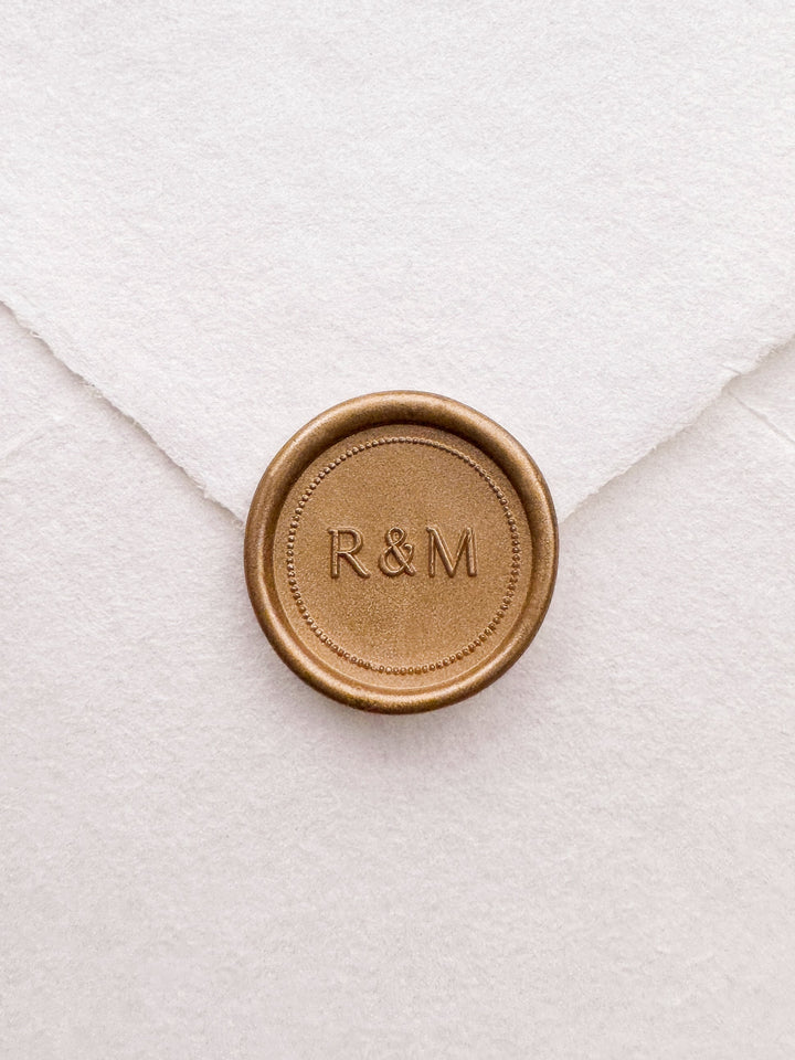 Gold monogram wax seal with a dotted border design