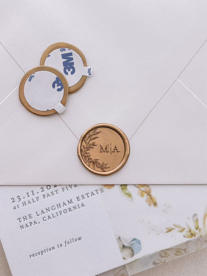 Gold personalized initials botanical monogram wax seal stickers with self-adhesive backings on a wedding invitation, beige envelope, and vellum jacket