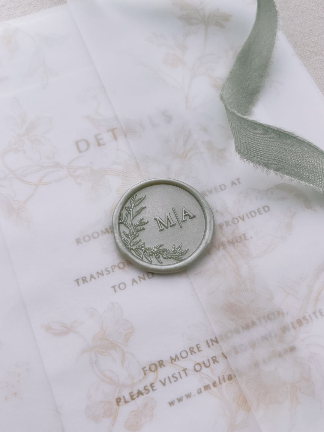 Light metallic sage green personalized initials wax seal featuring a custom botanical monogram on a wedding invitation vellum jacket